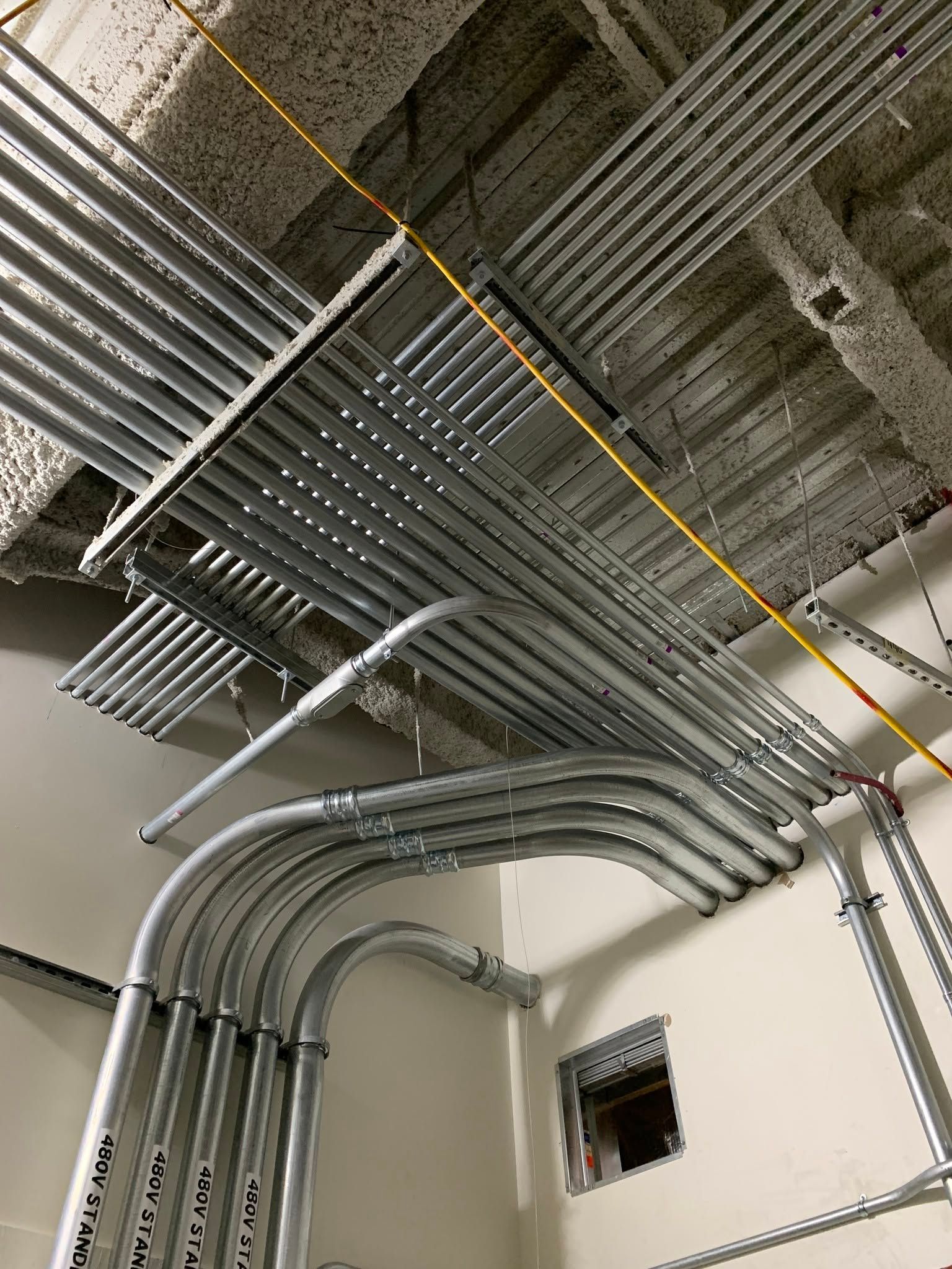 Metal electrical conduit and cable trays on a concrete ceiling in a utility room