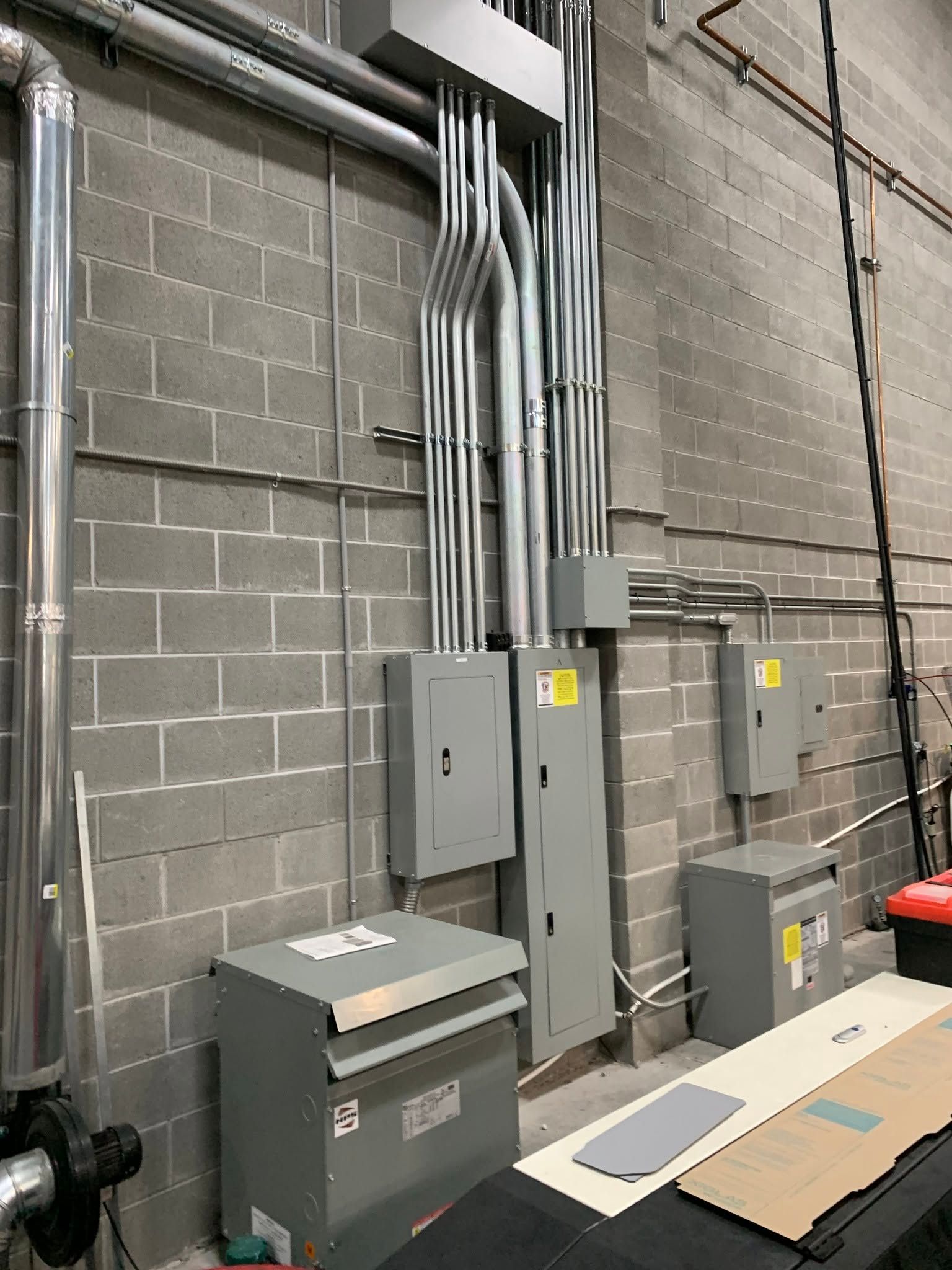 Industrial utility room with electrical panels, gray conduit pipes, and cinder block walls