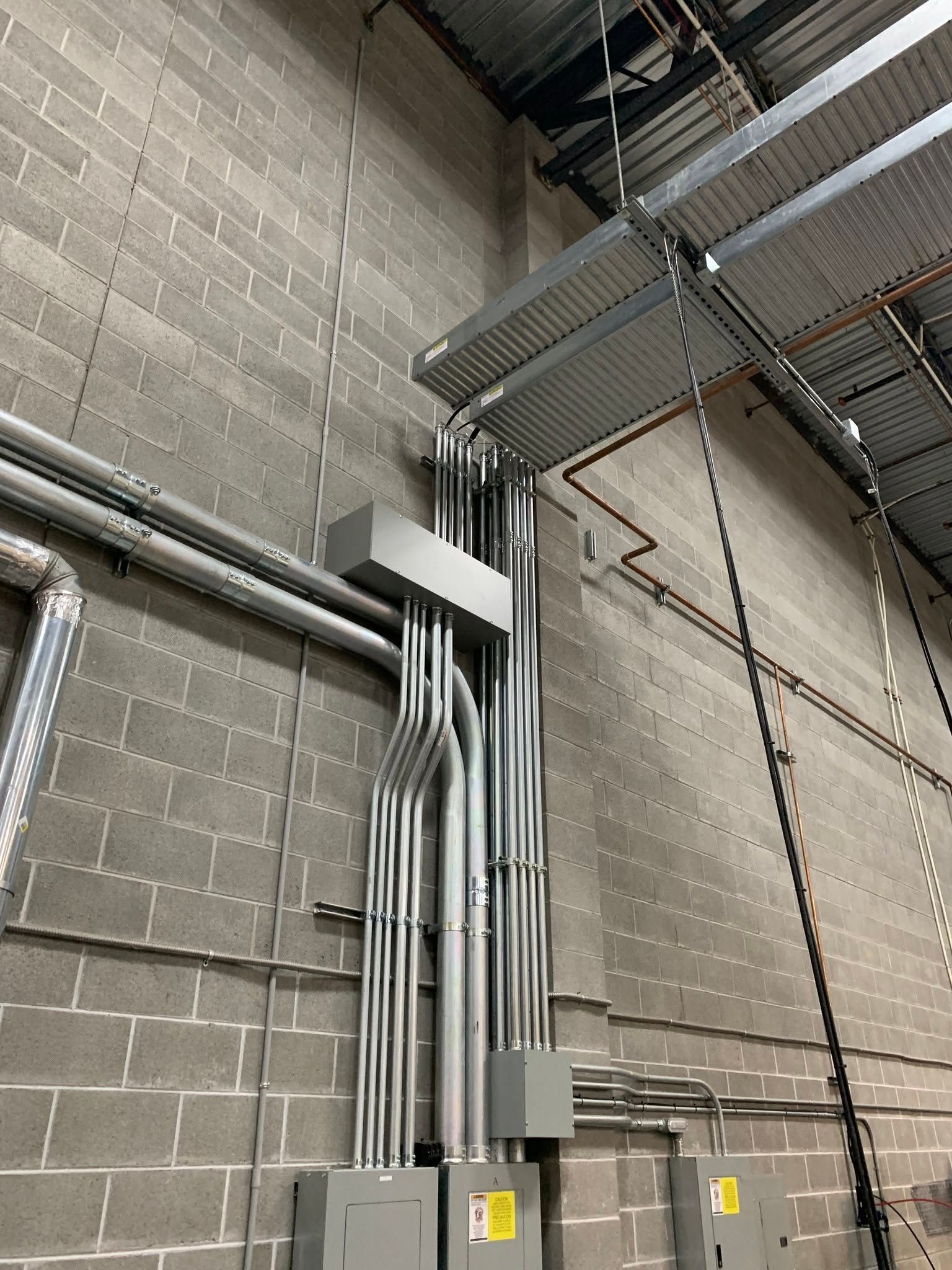 Industrial utility room with gray electrical conduits and metal cable trays on a concrete block wall
