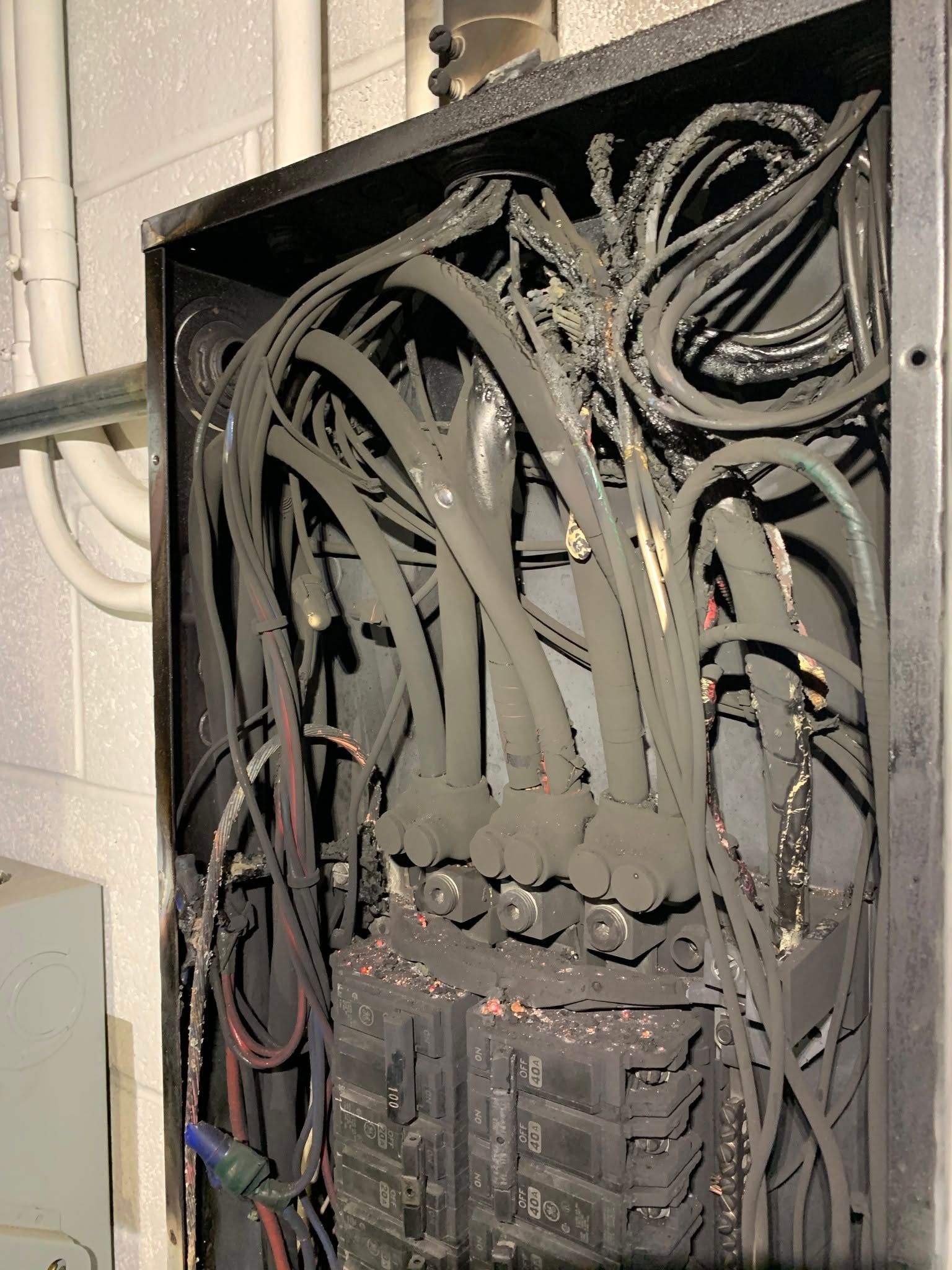 Open electrical panel with tangled black cables and circuit breakers inside.