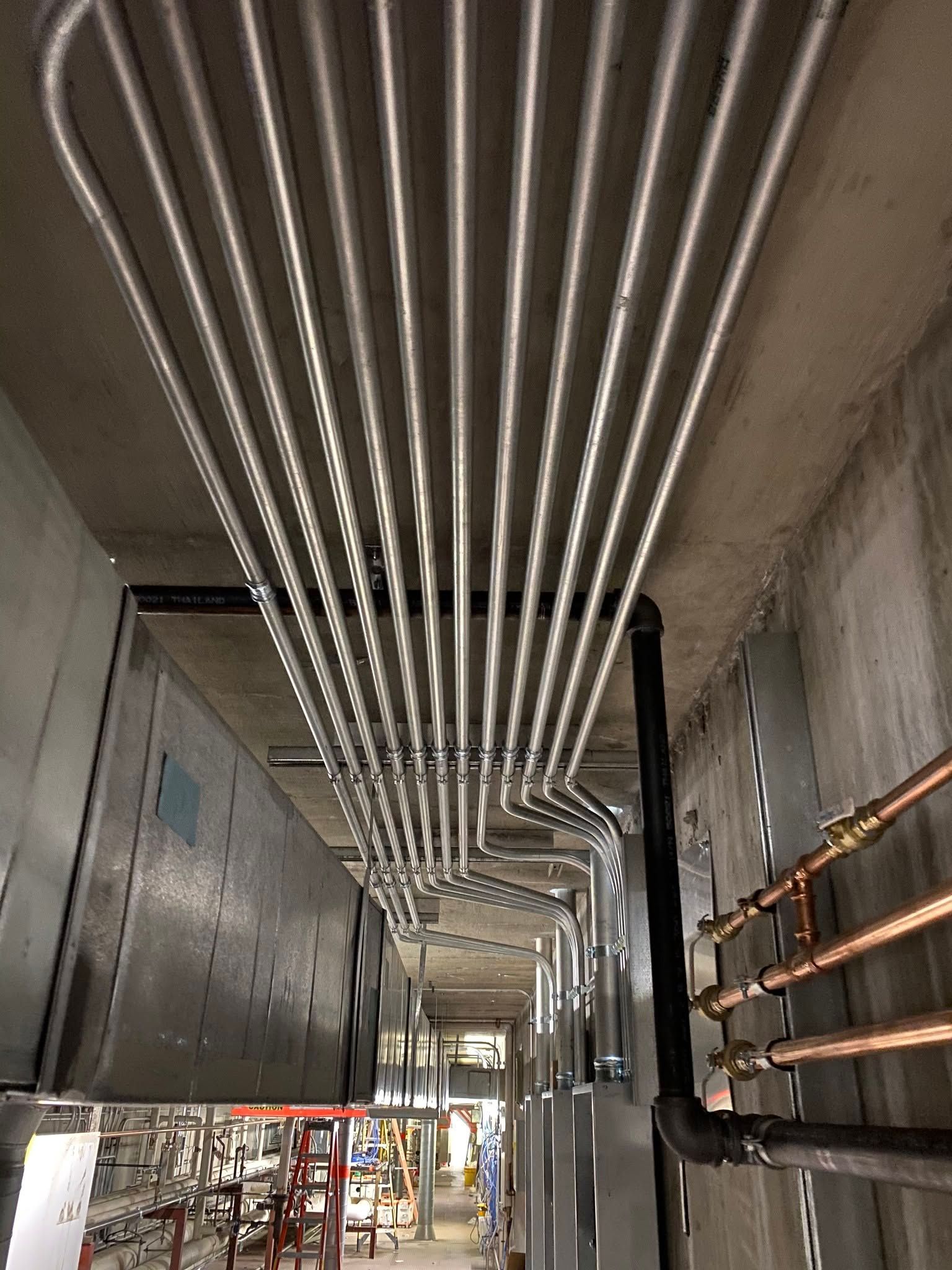Industrial hallway with exposed ceiling pipes and electrical conduits in a concrete building under construction