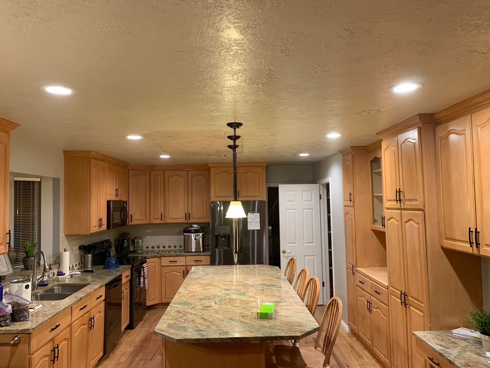 Wooden kitchen with granite island, pendant lights, and stainless steel appliances under warm ceiling lights