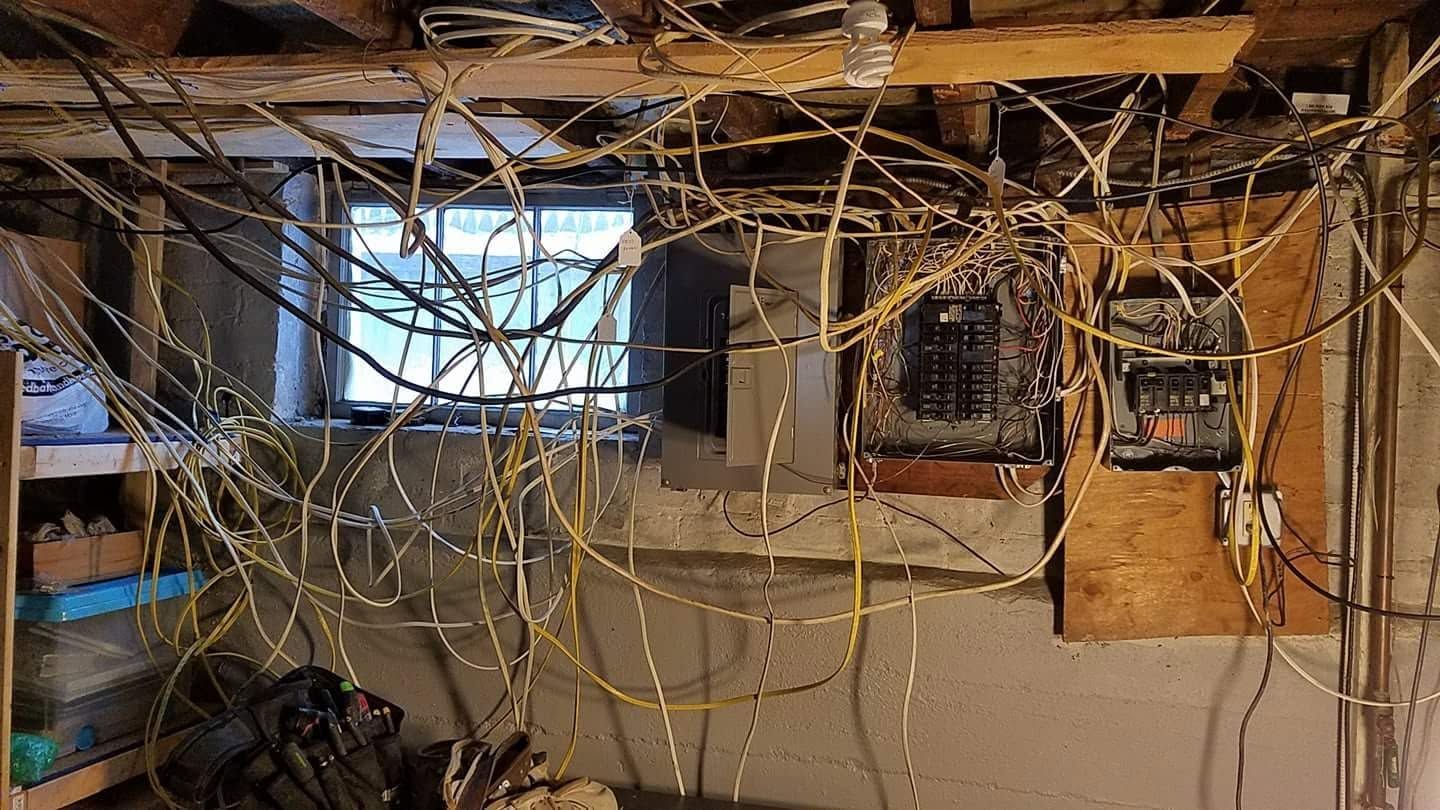 Basement ceiling with exposed wires, pipes, and electrical panels over a work area