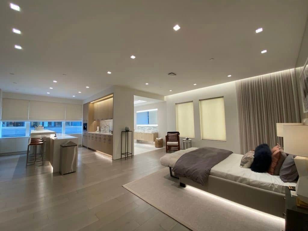 Modern open-concept bedroom and living area with a king bed, sofa, kitchenette, and soft recessed lighting