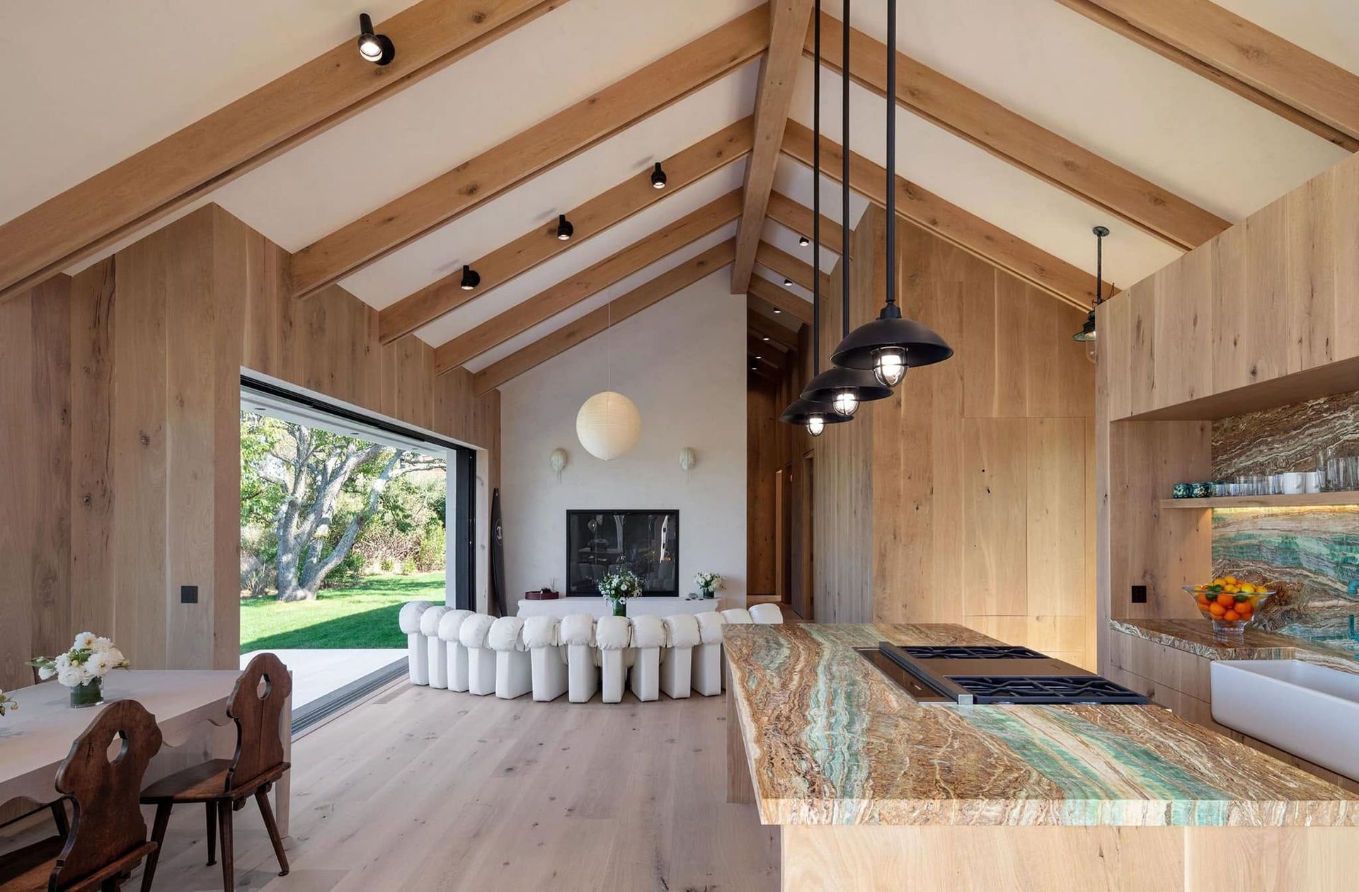 Modern open kitchen and dining room with wood beams, large windows, and a marble island