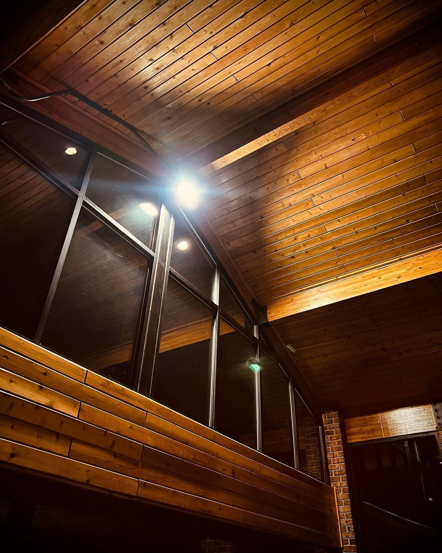 Wood-paneled interior with a bright ceiling light and large dark windows or glass panels