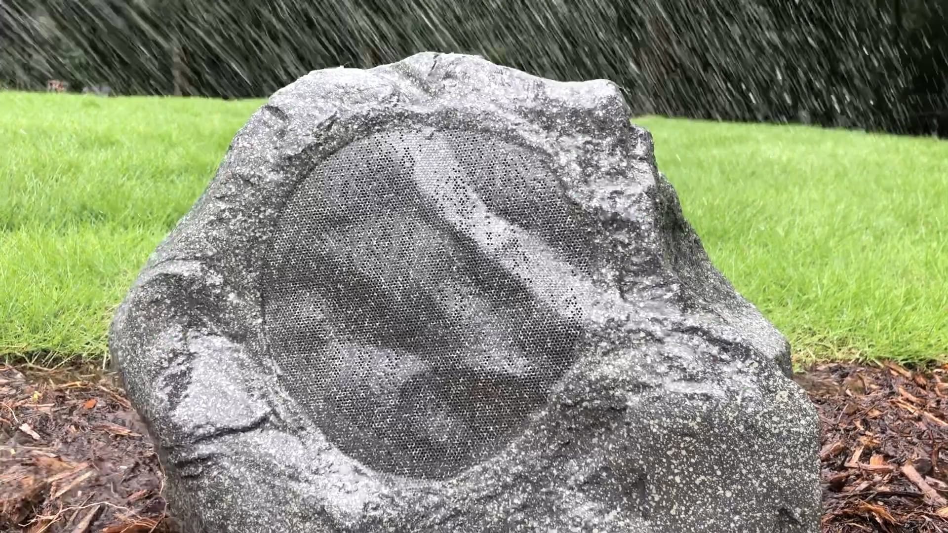 Large gray rock in a grassy garden with water spraying in the background