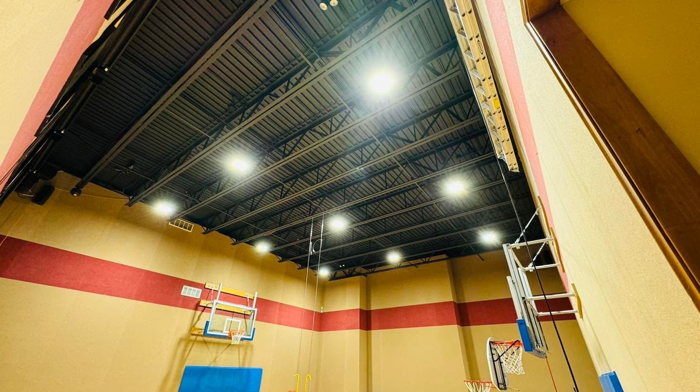 Indoor gym ceiling with exposed beams, bright lights, and yellow walls with a red stripe