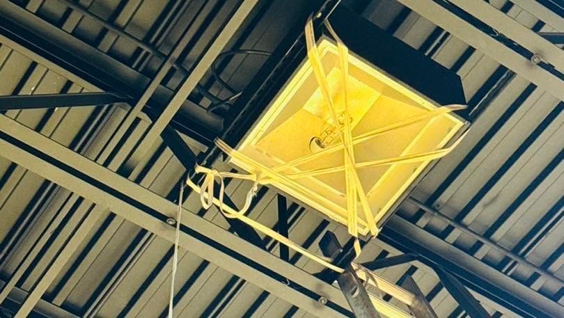 Yellow hanging light fixture in an industrial ceiling with exposed beams and ducts
