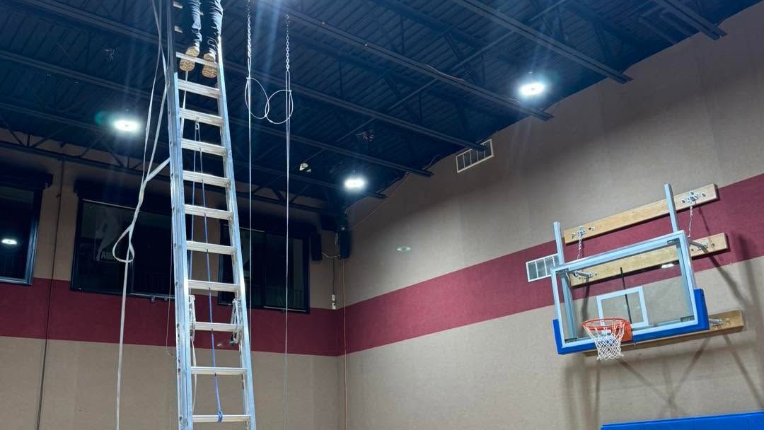 Indoor gym with a tall ladder reaching the ceiling beside a basketball hoop.