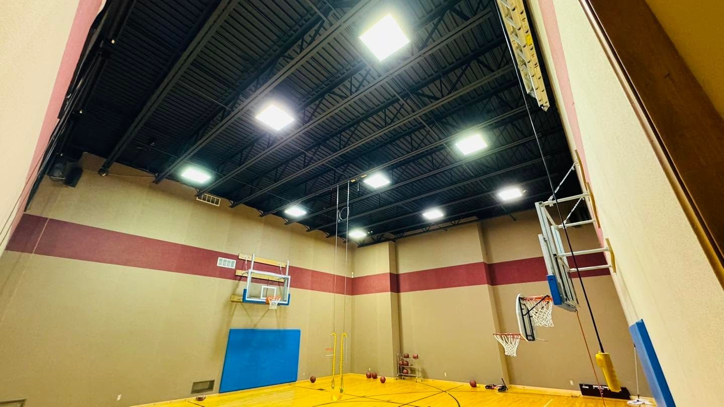 Empty indoor gymnasium with high ceiling, bright lights, blue wall mats, and basketball hoops