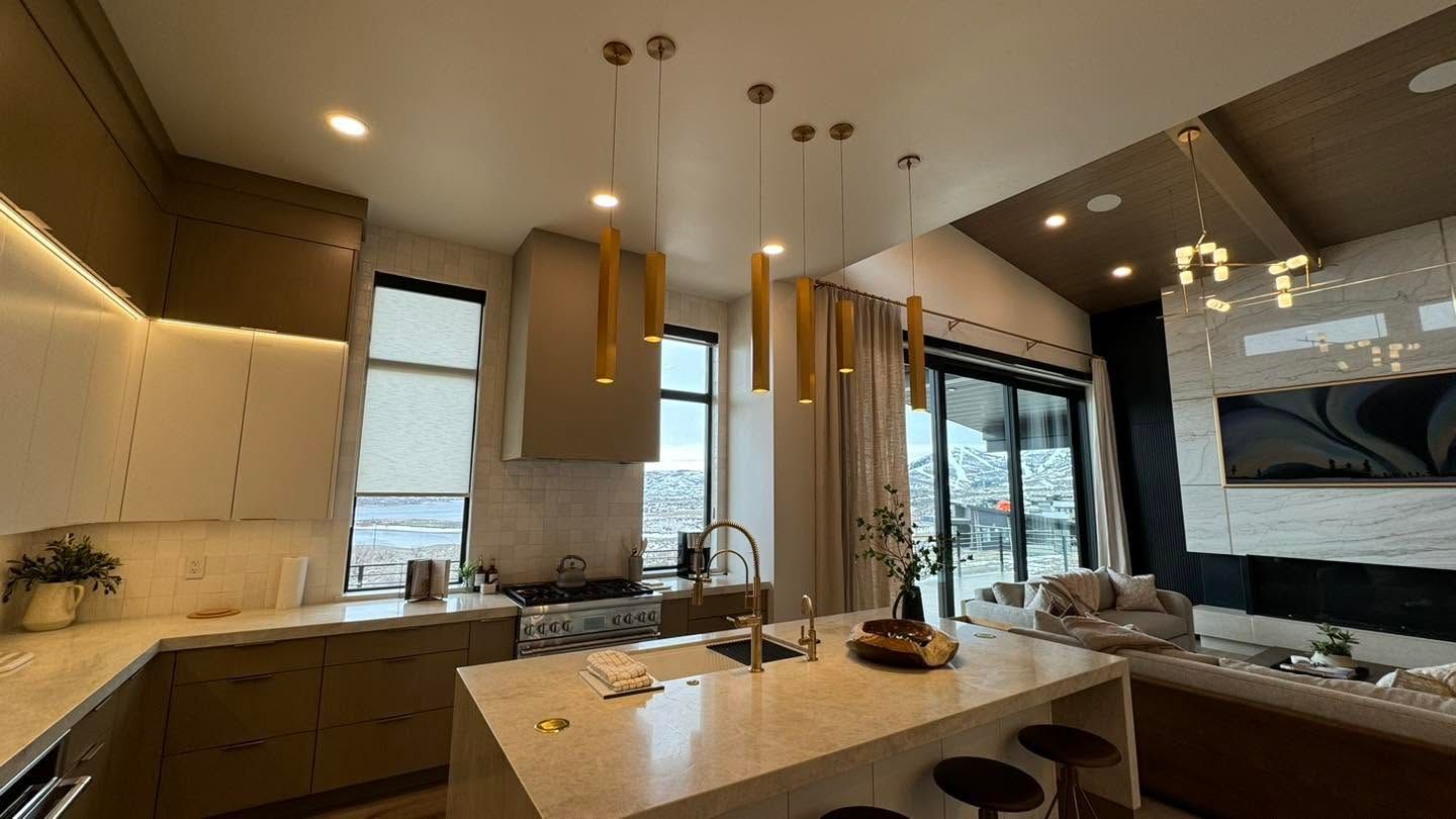 Modern kitchen with island, pendant lights, white cabinetry, large windows, and a view into the living area