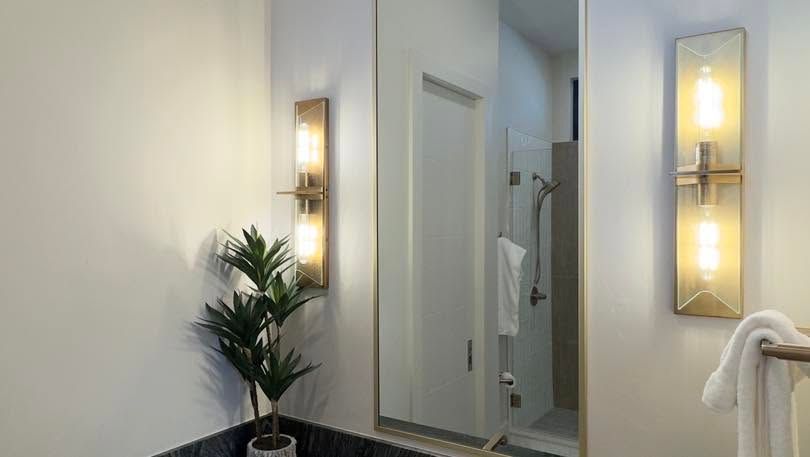 Bright bathroom with wall sconces, a mirror, white towels, and a potted plant by the sink.