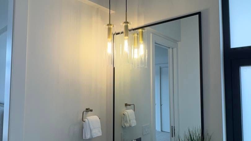 Modern bathroom with a large mirror, pendant lights, white towels, and a doorway visible in the reflection