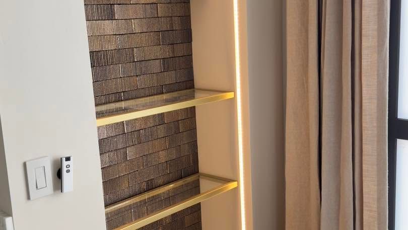 Built-in wall shelves with warm lighting beside beige curtains and a window