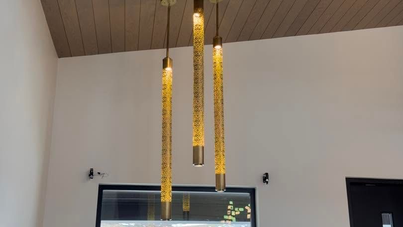 Three gold pendant lights hang from a wooden ceiling over a doorway in a modern room.