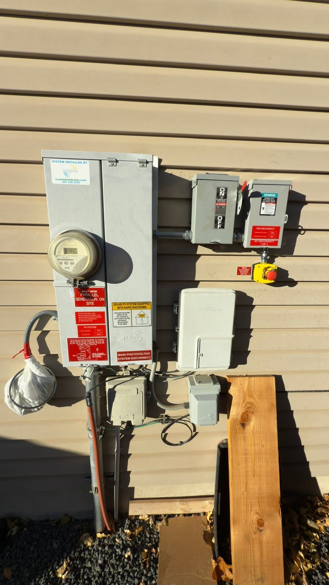 Two utility meters and electrical boxes mounted on tan house siding beside a wooden post.
