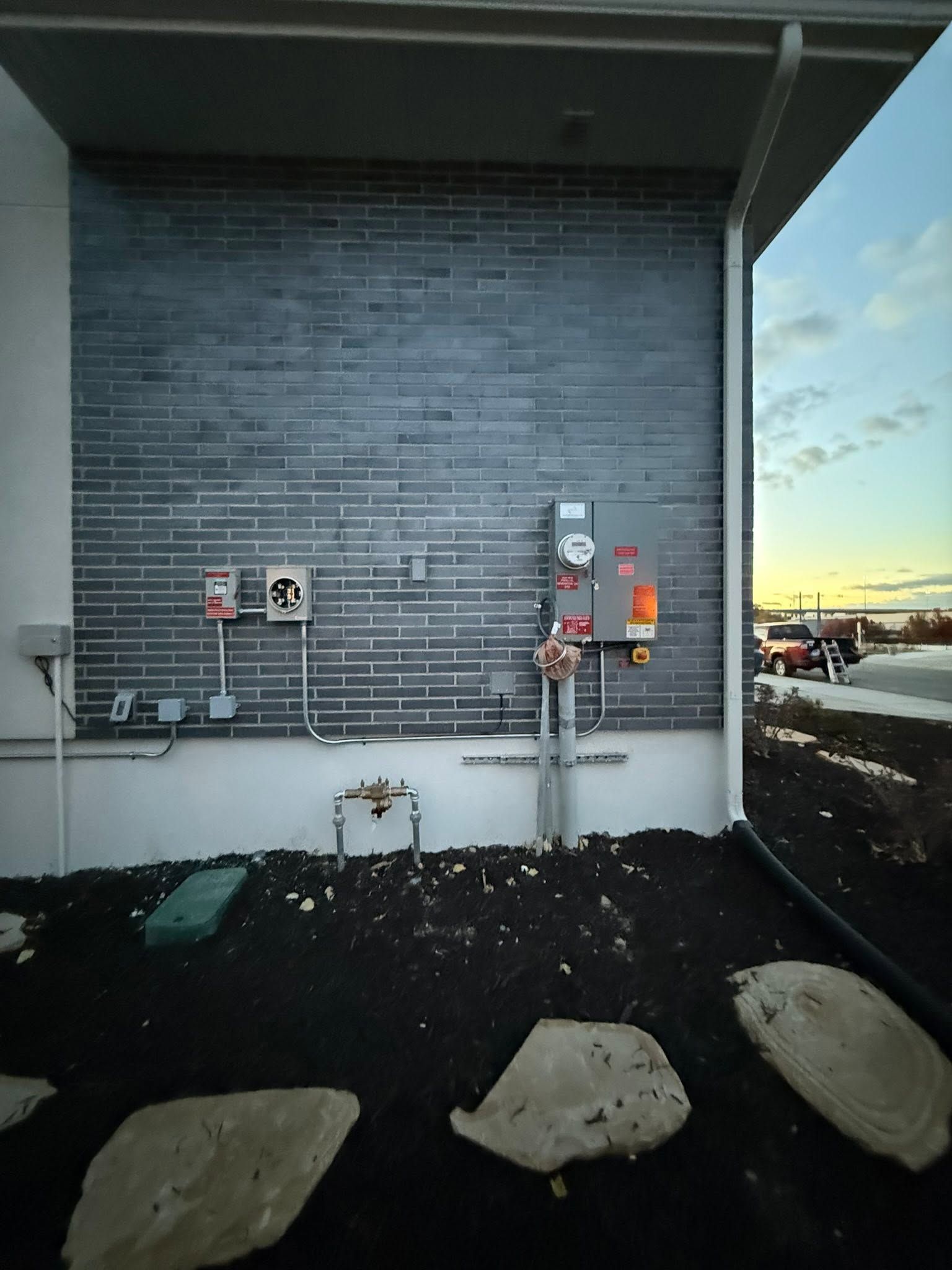 Outdoor utility wall with meters and pipes beside a building entrance at sunset.