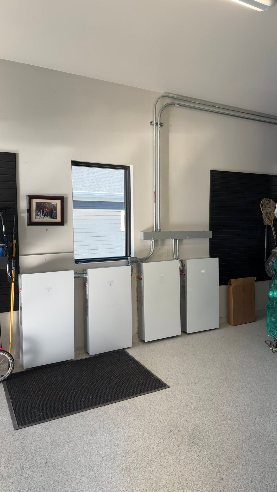 Garage interior with white cabinets, a window, wall art, a floor mat, and exposed piping.