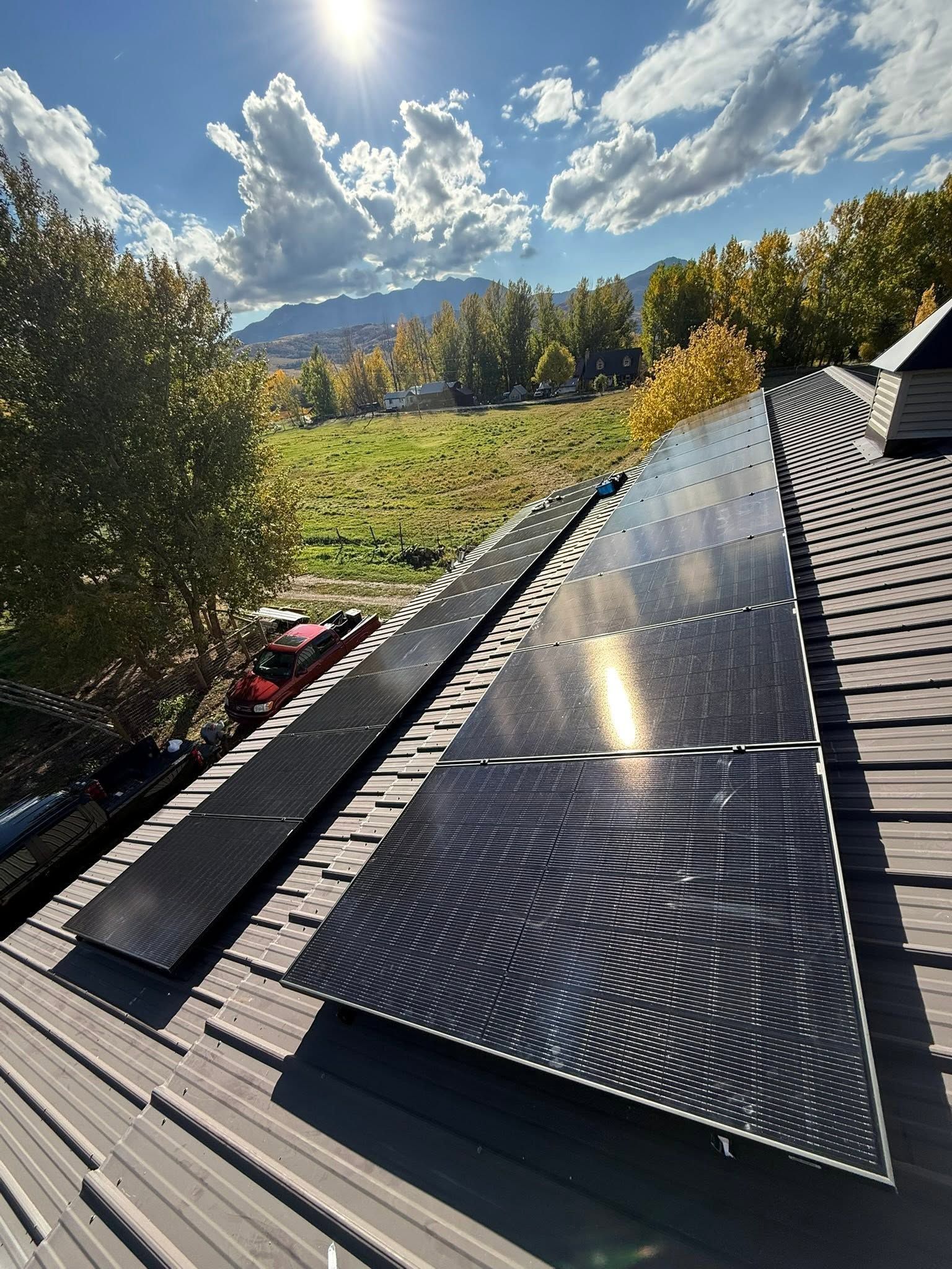 Solar panels on a sloped roof under a bright cloudy sky with mountains in the background