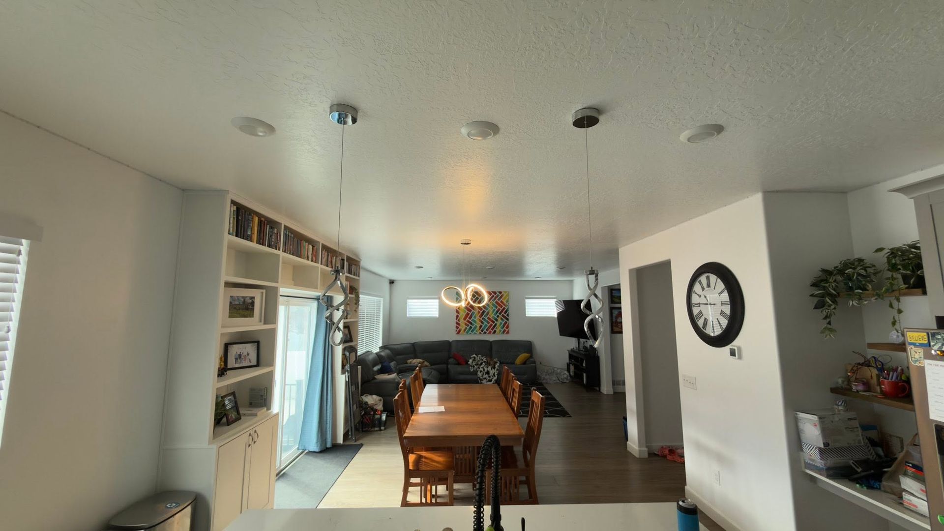 Modern kitchen and dining area with wooden table, white walls, and a wall clock.