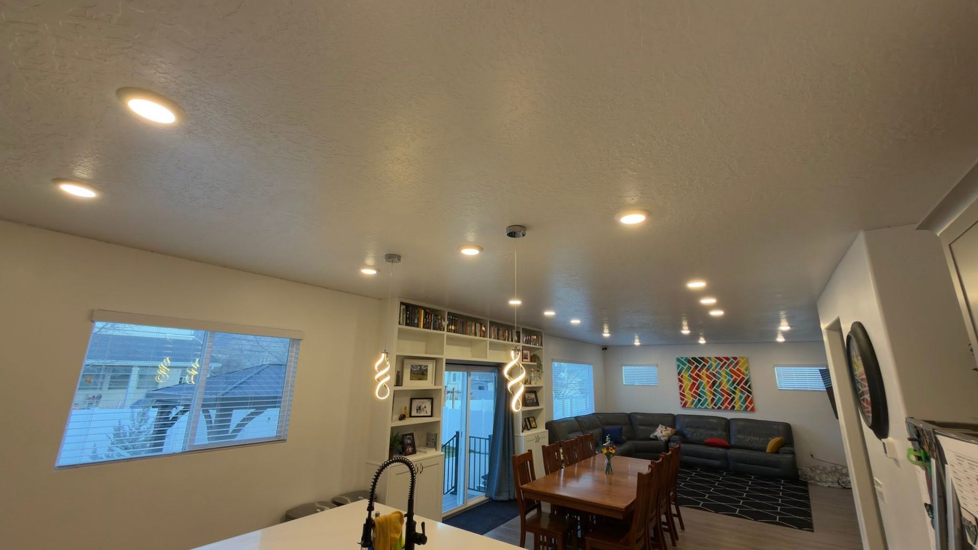Modern open-plan kitchen and dining area with recessed lights, wooden table, couch, and wall art