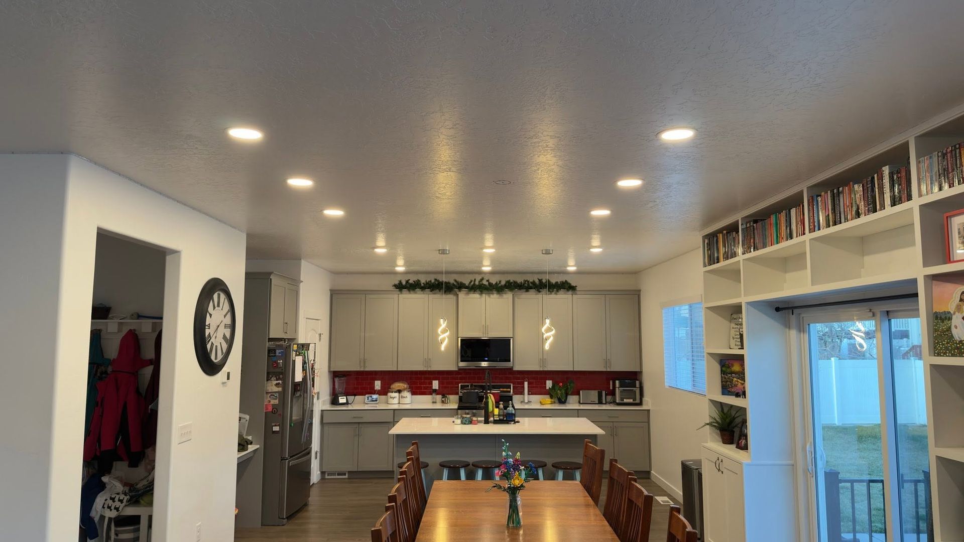 Bright open kitchen and dining area with white cabinets, red backsplash, and a long wooden table.