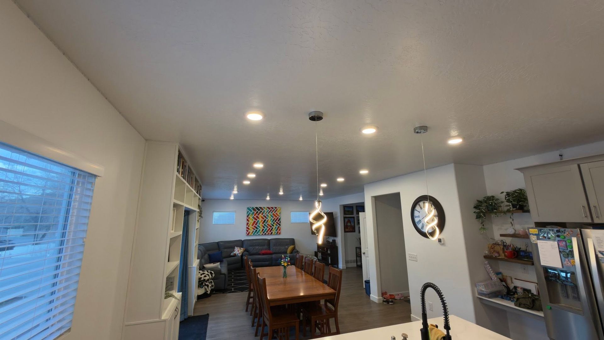 Bright modern kitchen and dining area with wood table, recessed lights, and a person in the background.