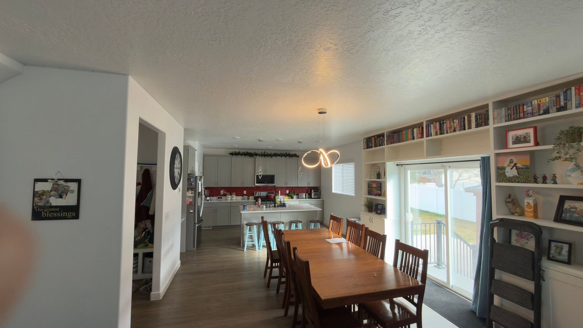 Dining room with a wooden table, chairs, wall art, and a view into a bright kitchen and living area.