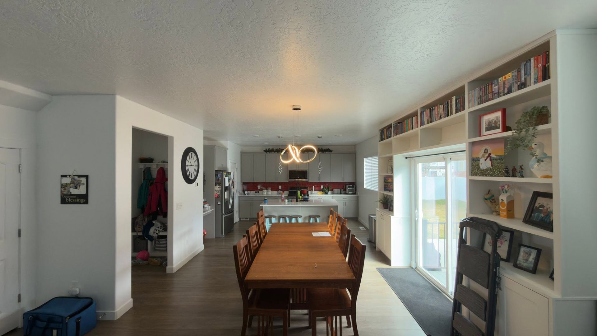 Bright dining room with wooden table, white shelves, and a glass door opening to a sunlit patio.