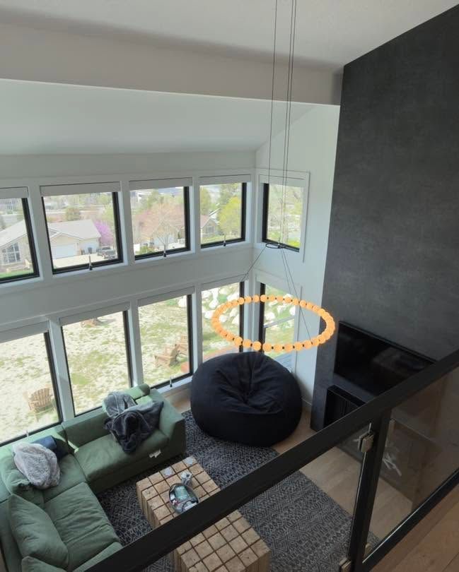Modern living room with large windows, green sofa, black beanbag, and hanging chandelier overlooking trees
