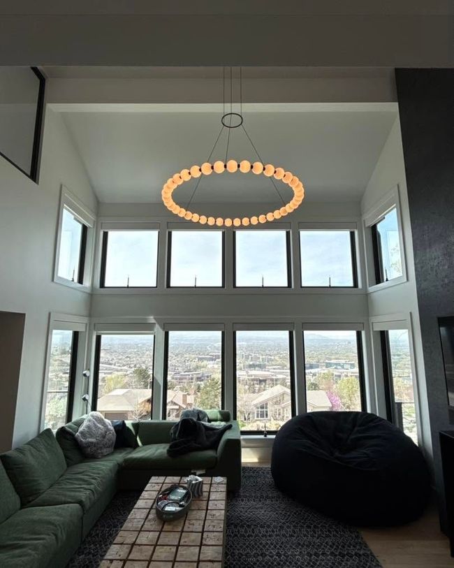 Modern living room with tall windows, green sofa, black beanbag, and circular chandelier above.