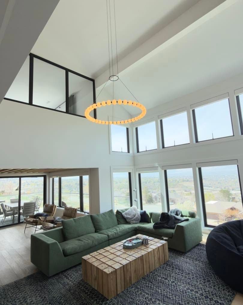 Bright modern living room with green sectional, wood coffee table, and floor-to-ceiling windows.