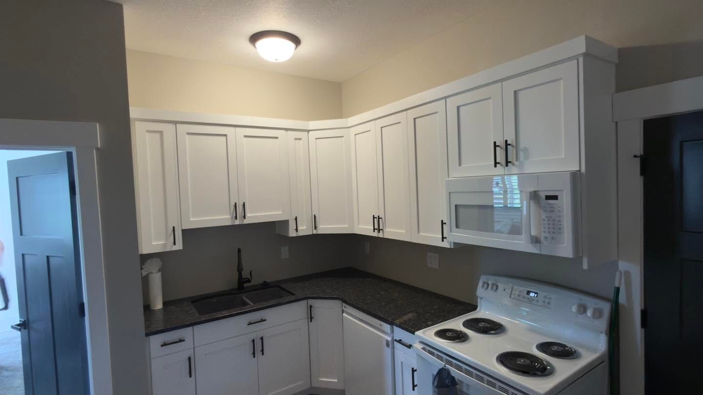 White kitchen with cabinets, black countertops, and a white stove under a ceiling light