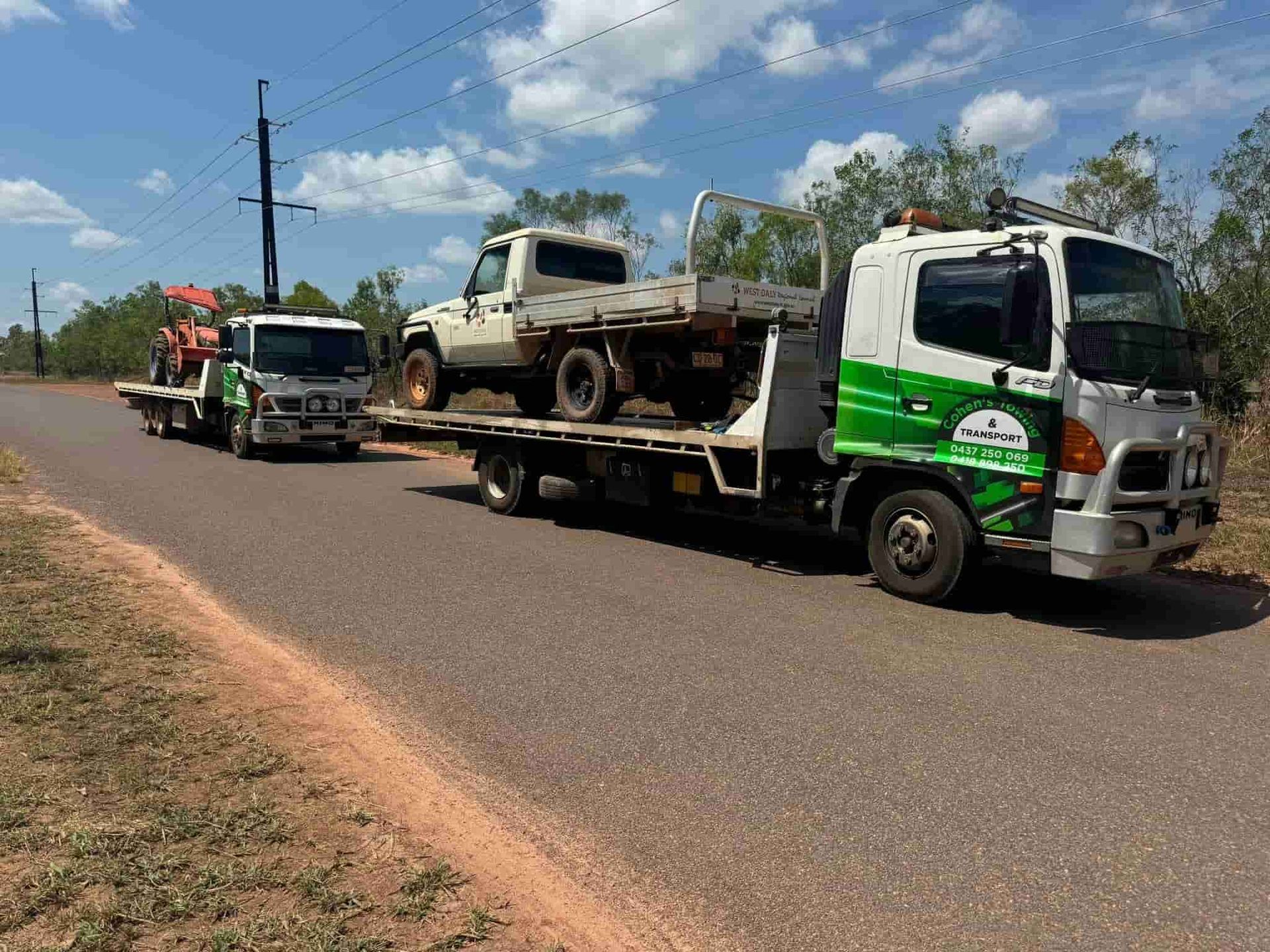 A Tow Truck is Carrying a Truck and a Tractor Down a Road — Cohen’s Towing & 4WD Recoveries In Winnellie, NT