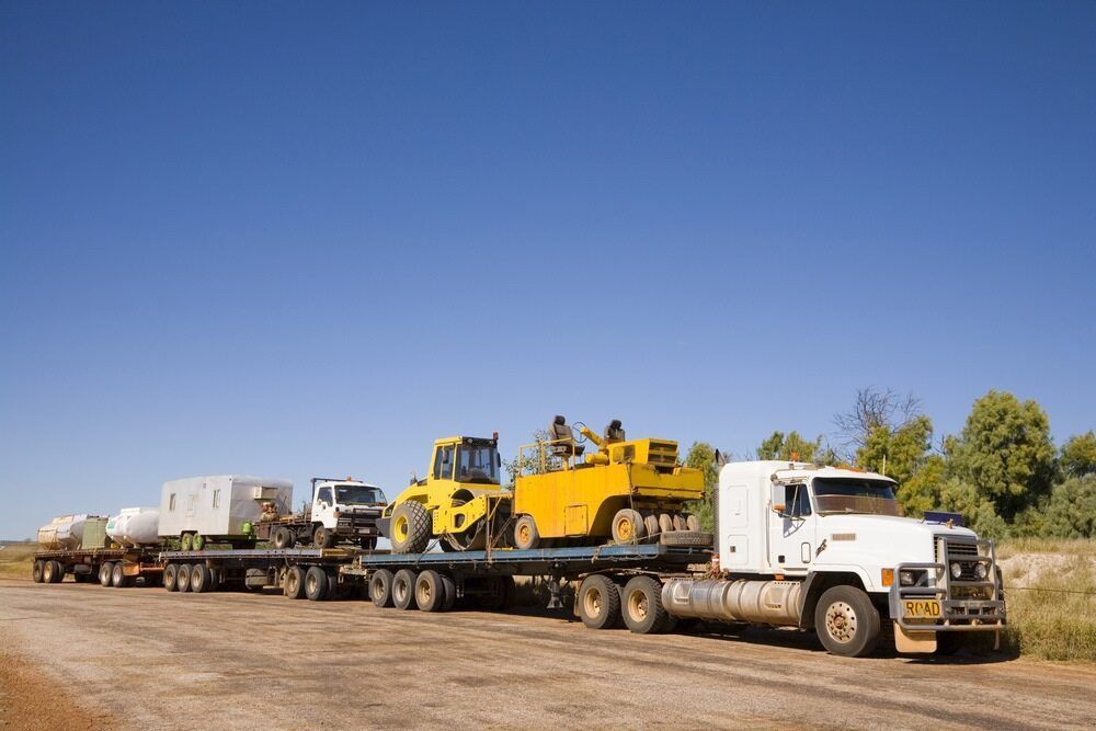 A White Semi Truck is Carrying a Yellow Tractor on a Flatbed Trailer — Cohen’s Towing & 4WD Recoveries In Katherine, NT