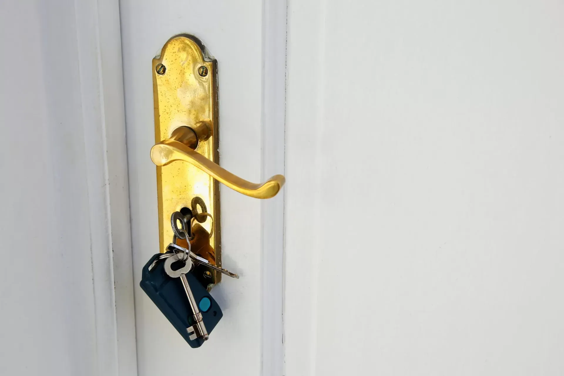 Gold door handle with keys hanging on it against a white door