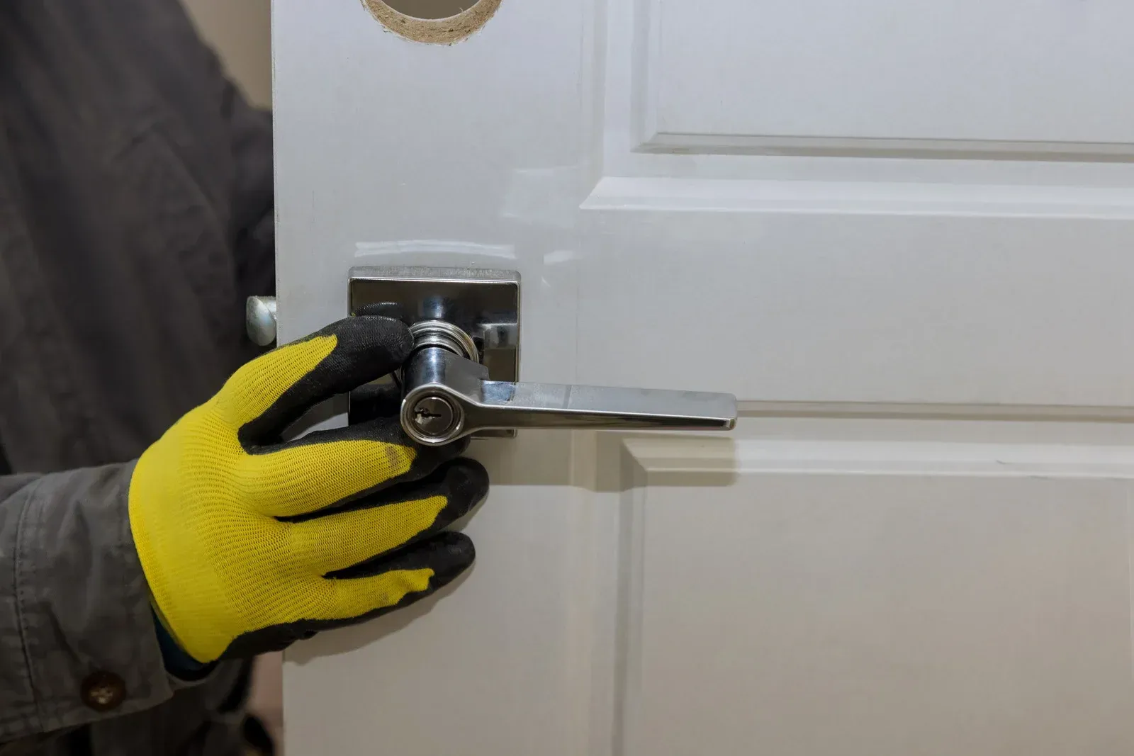 Gloved hand using a drill to install a door lock on a white door