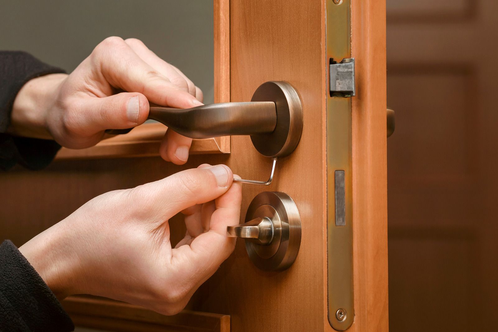 Hands unlocking a wooden door with a silver lock and handle