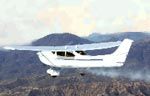 a small plane is flying over a forest with mountains in the background .