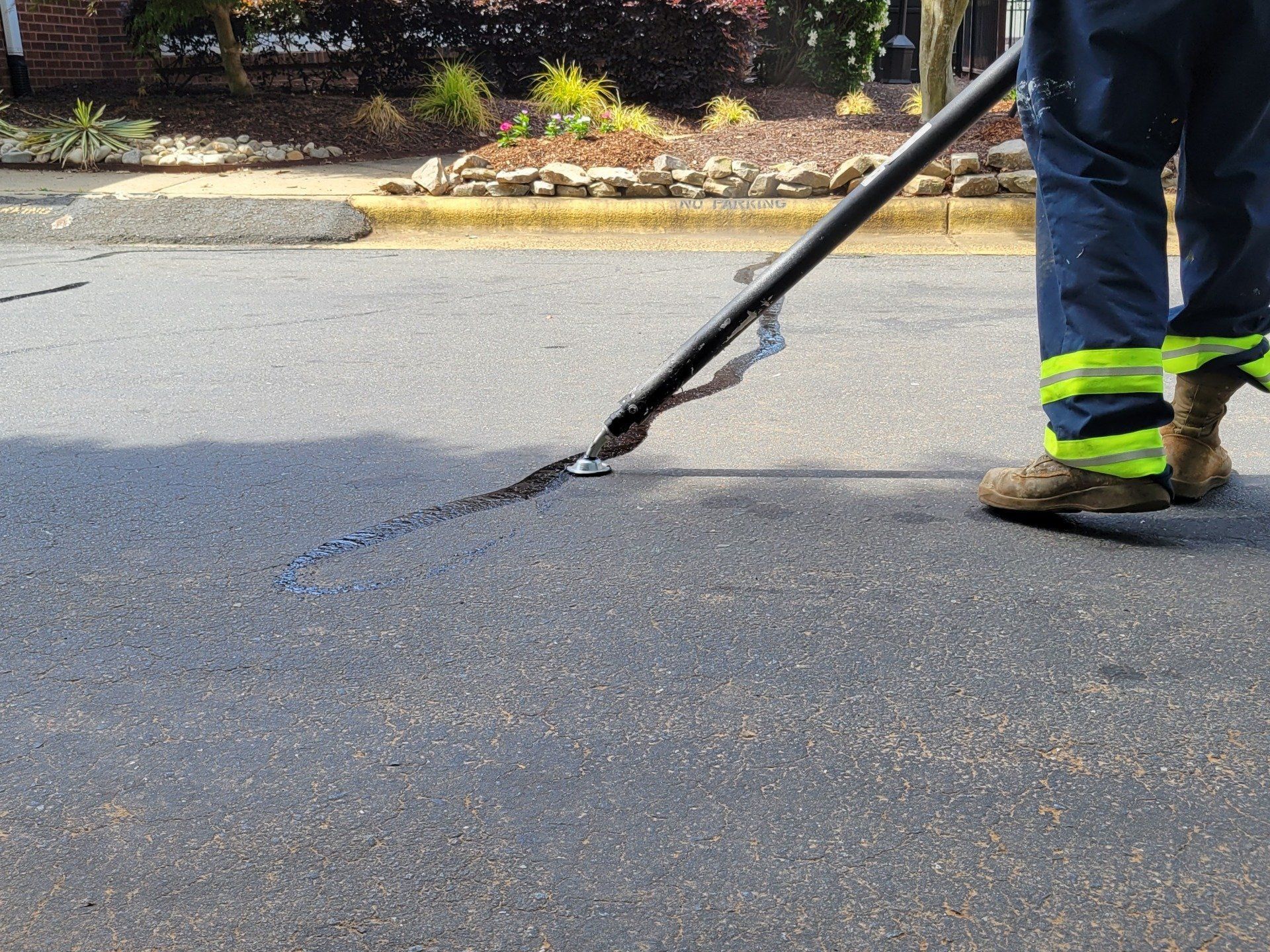 Worker sealing a crack in the road with a long black applicator