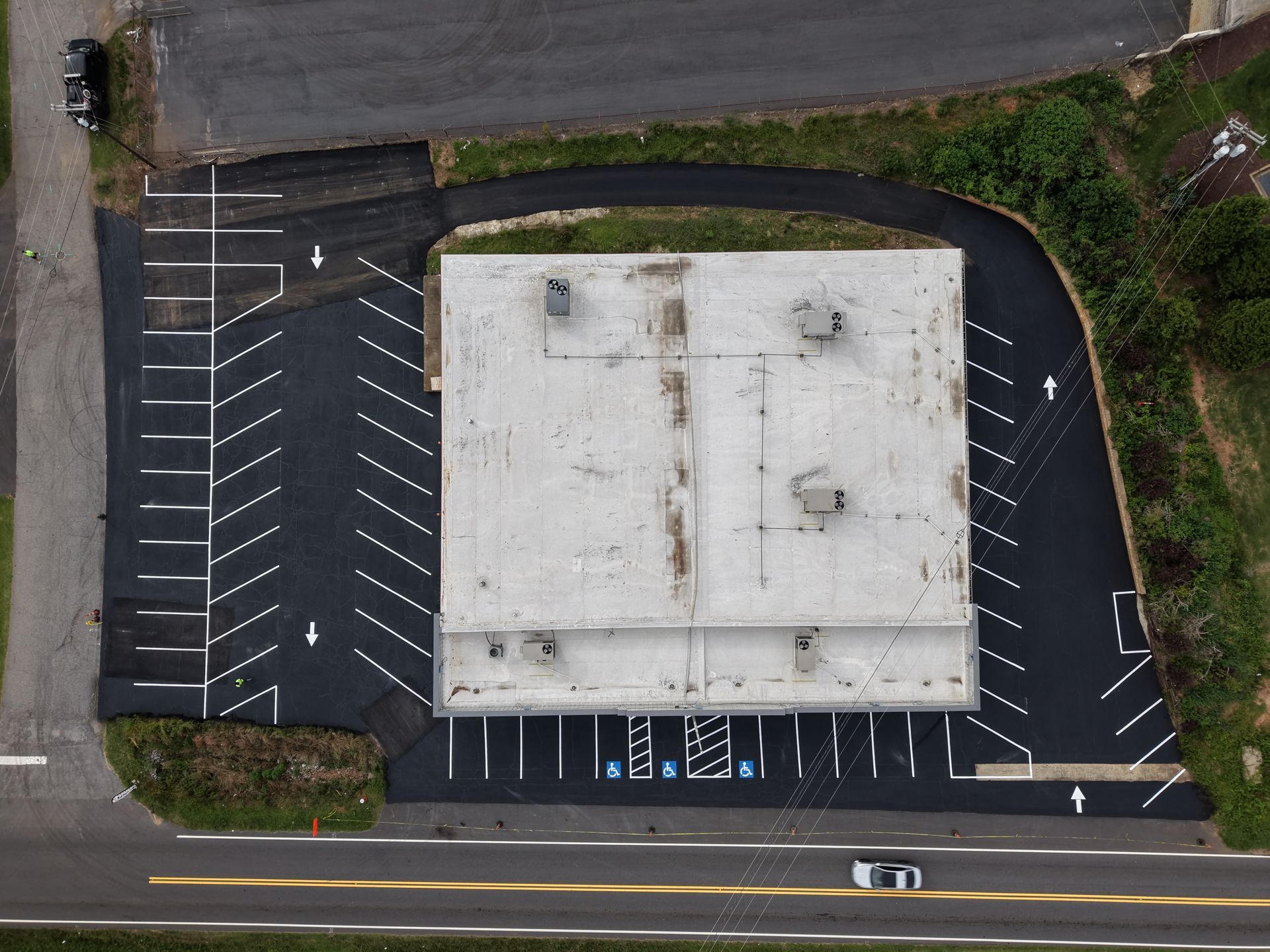 An aerial view of a rectangular warehouse building surrounded by a newly paved asphalt parking lot with white marked spaces.