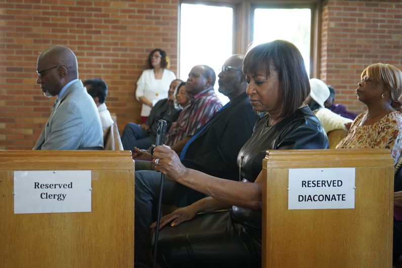 A group of people sits in church pews labeled 