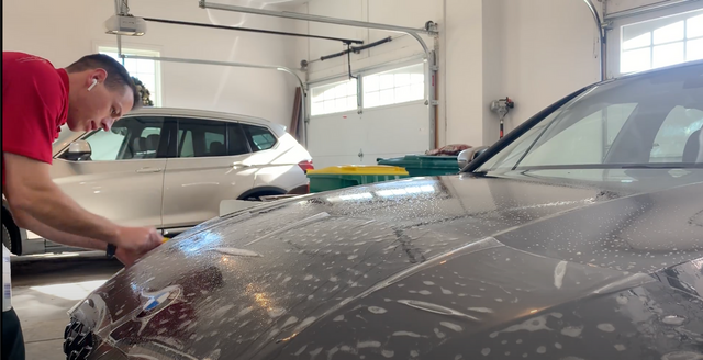 A man is cleaning the hood of a car in a garage.