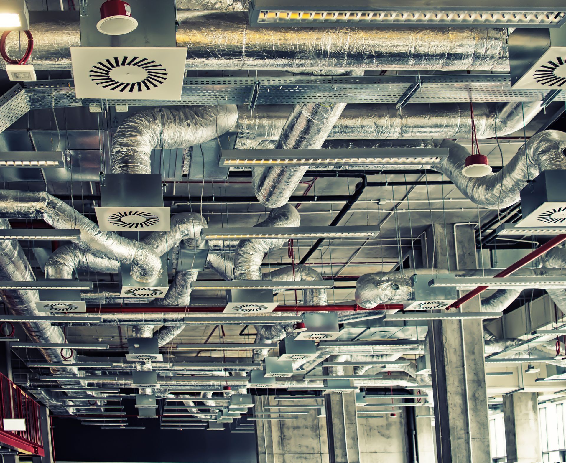 Industrial ceiling with exposed silver ducts, pipes, and vents in a building interior.