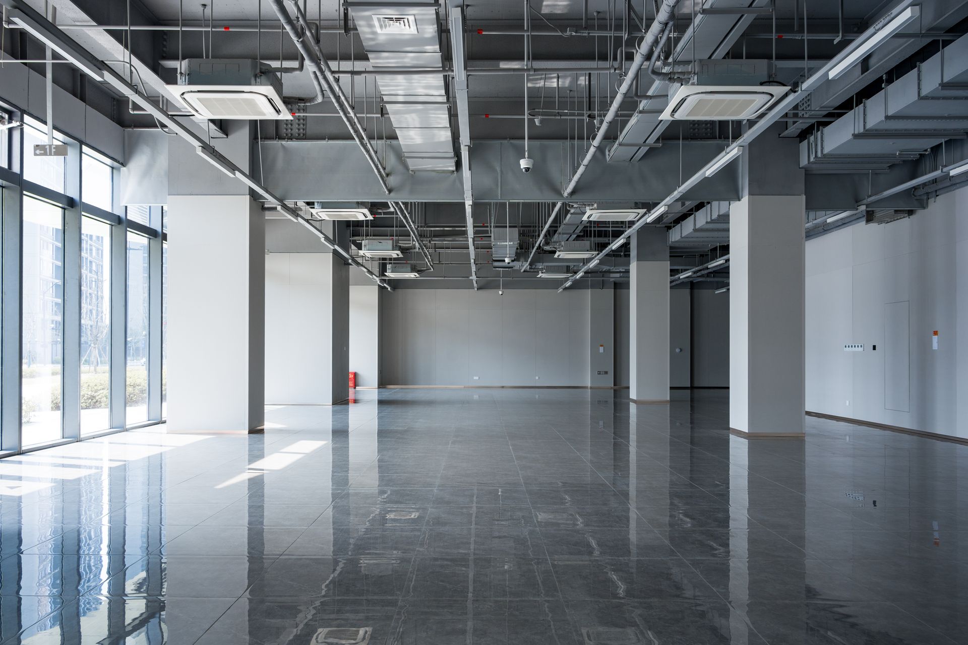 Empty modern office space with large windows, exposed ceiling ducts, and glossy black floors