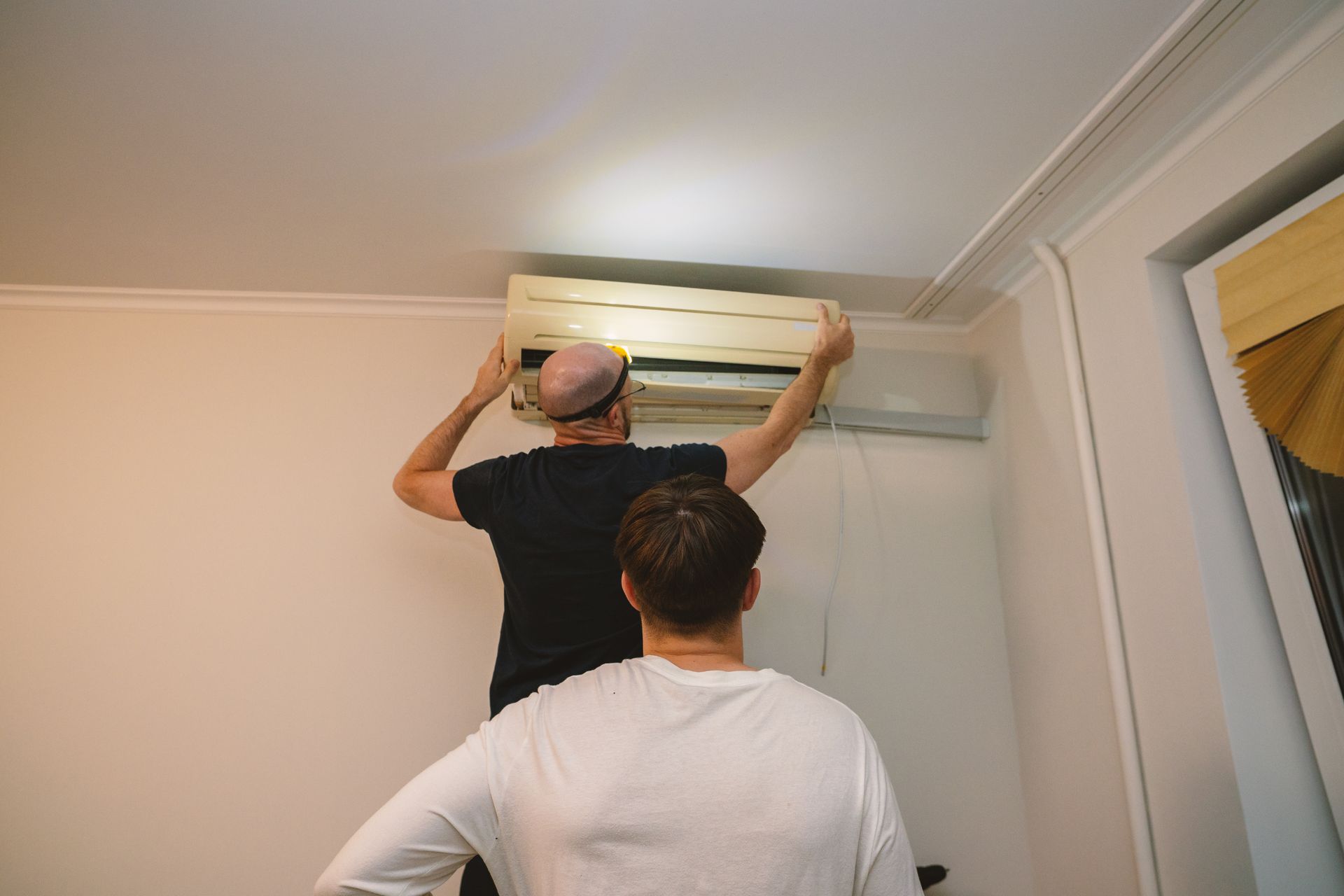 Two people installing or adjusting a wall-mounted air conditioner in a room Two people installing or adjusting a wall-mounted air conditioner in a room