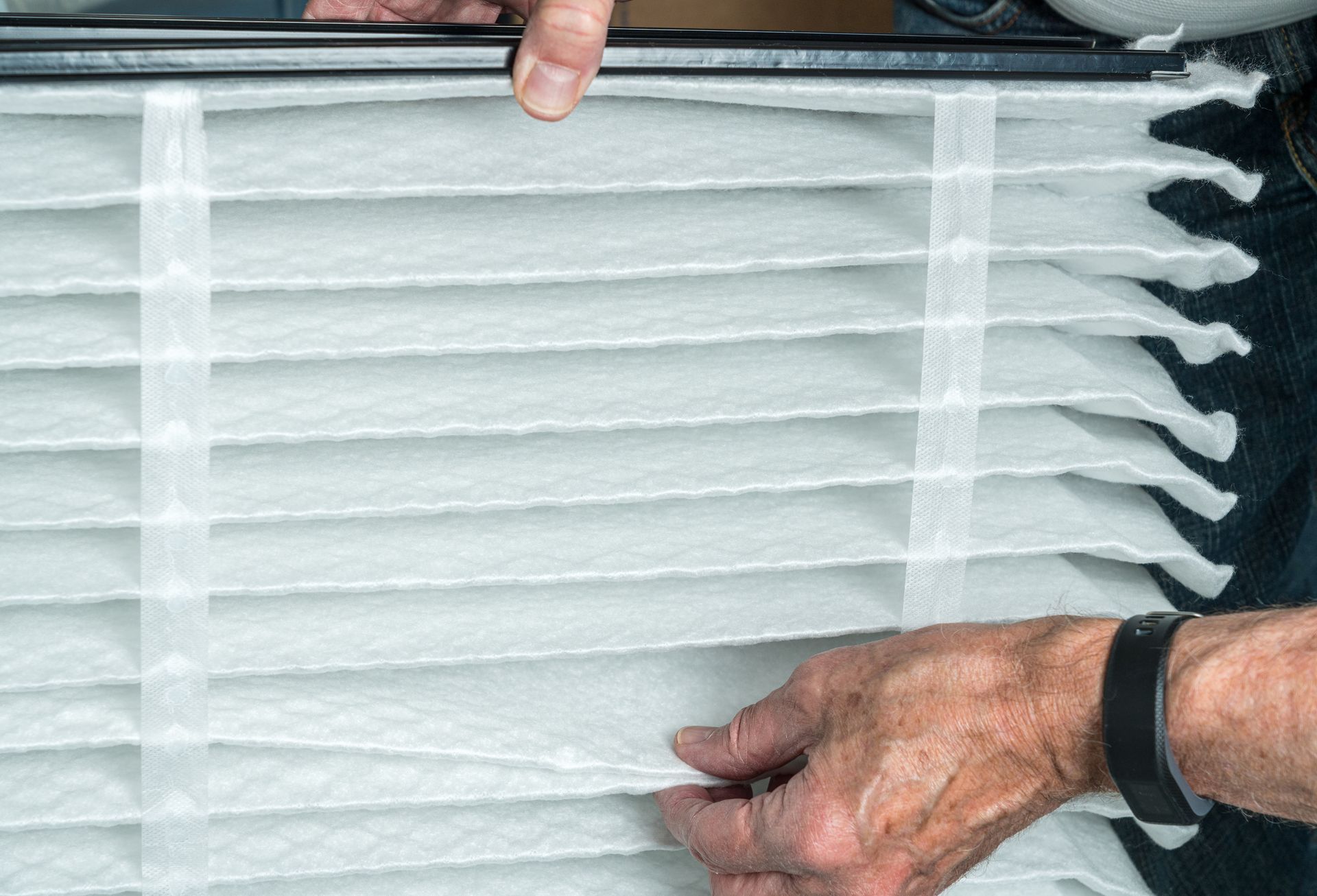 Hands adjusting a white pleated air filter in a vent frame Hands adjusting a white pleated air filter in a vent frame