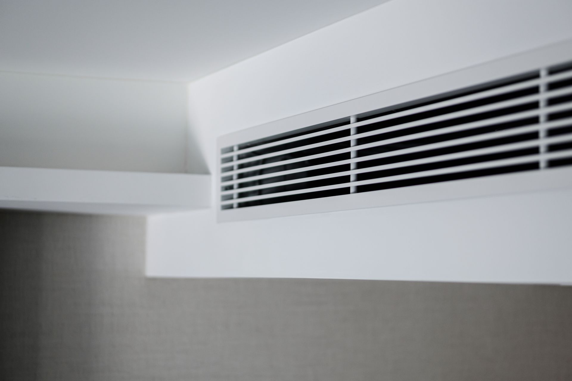 White ceiling air vent with horizontal slats above a gray wall panel White ceiling air vent with horizontal slats above a gray wall panel
