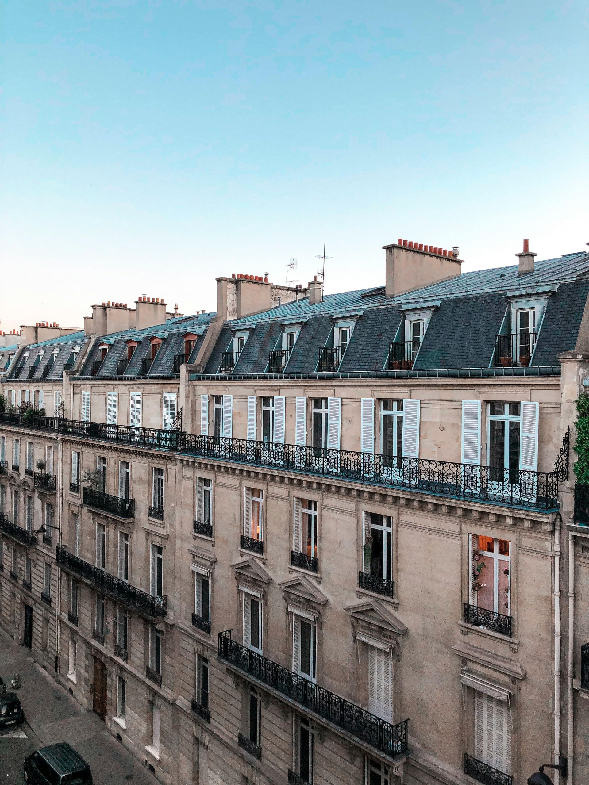 Une personne nettoie une lucarne sur un toit de tuiles rouges. Une échelle est appuyée contre la maison. Journée ensoleillée.